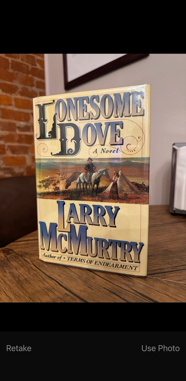 The phone camera's Use Photo screen showing the dust jacket of Lonesome Dove by Larry McMurtry on a wooden table.